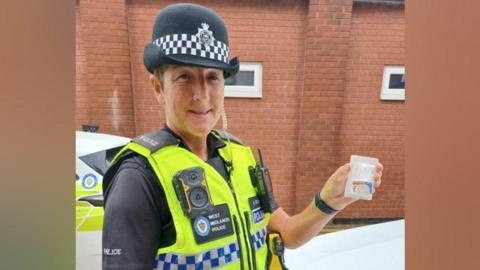 PC Kirstie Brooks in a fluorescent yellow police vest, and black police hat. 