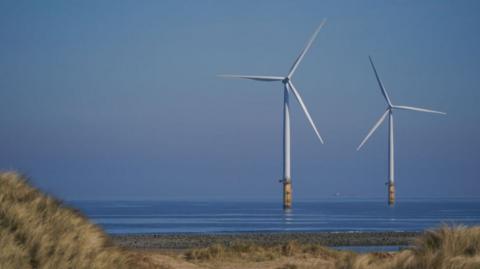 Two wind turbines are in the water in the distance at an offshore wind farm at South Gare near Redcar. 