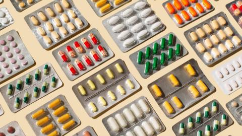 A stock image of many medications laid out in blister packs on a pale-coloured table.