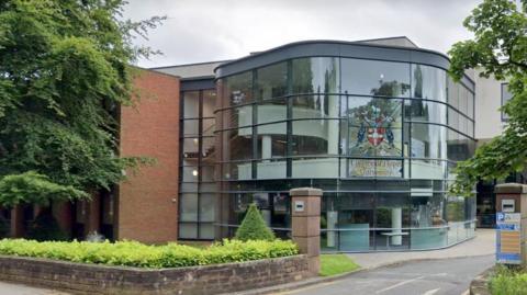 A glass-fronted building set behind a sandstone wall entrance. A stained glass panel features the writing Liverpool Hope University along with the academic institution's crest.