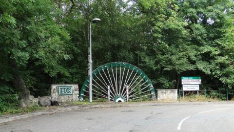 An old pit wheel  - in green - by the side of a road