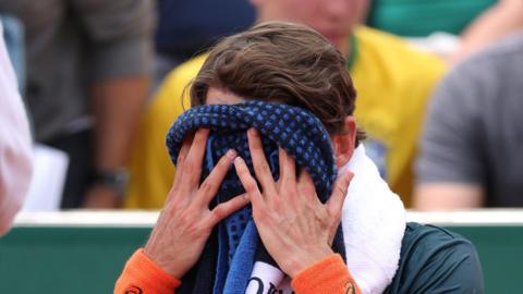 Alex de Minaur covers his face with a towel at the French Open