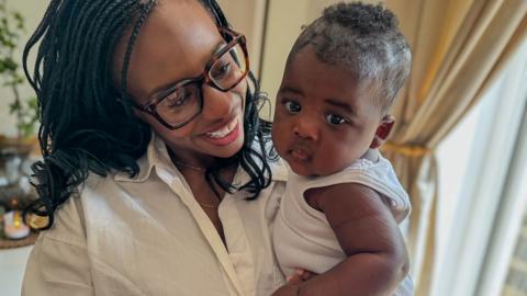 A smiling mum in glasses holds her young baby.