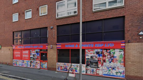 Exterior of Wines and Spirits KSP. It has red signage and multiple advertisements on the windows. 