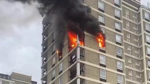 Fire pours out of the windows on two sides of a grey concrete tower block as thick black smoke engulfs the floors above the blaze. One floor of the block is alight. 
Pic is from UGC  - Leslie (doesn't want to give a surname)