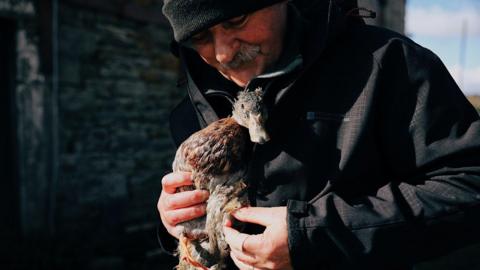 Tony Johnson holding a duck. He is wearing a dark coat and a beanie hat.