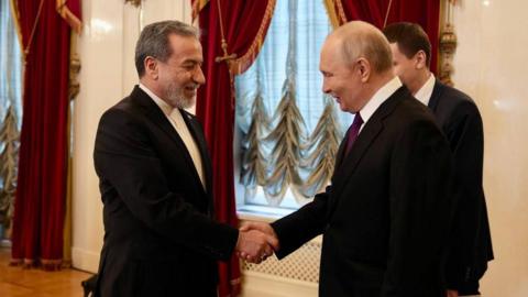 Iran's foreign minister Abbas Aragchi and Putin shaking hands, both wearing suits.