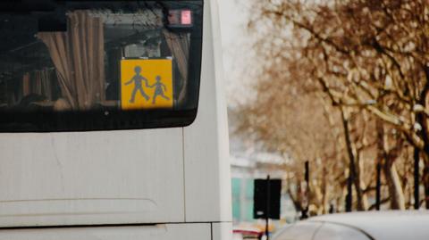 A stock image showing the back of a white coach with a yellow school bus icon fixed to the window.