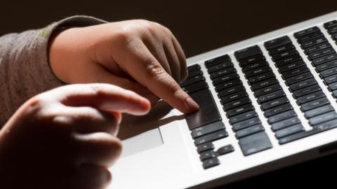 Illustrative library photograph showing the hands of a young child typing on the keyboard of a laptop.