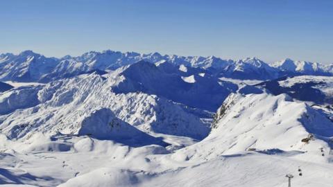 A white snowy mountainous landscape with a blue sky above is captured from the top of La Plagne ski resort in France.