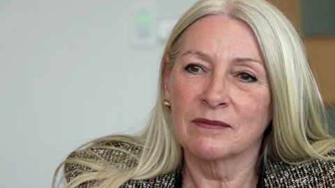 Kay Mason Billig is looking at the camera. We can see she's wearing a patterned suit jacket.