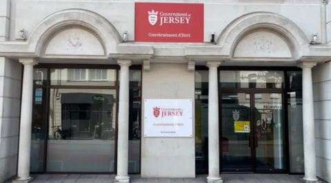 The front of the Government of Jersey office, which has a red sign saying Government of Jersey above and then a white version directly below, in between two curved glass doors.