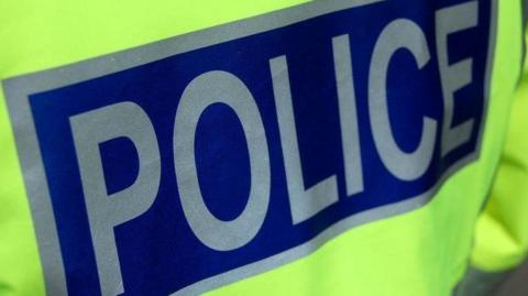A close up of a high visibility police jacket. the word "police" is in silver capital letters against a blue background.