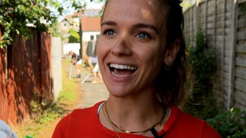 Woman smiles while people clean up alleyway in background