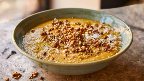 A greenish bowl full of smooth lentil soup with crispy seed topping
