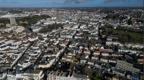 An ariel view of St Helier in Jersey. Dozens of rows of houses are visible under a blue sky.