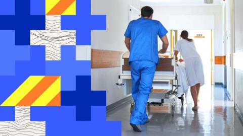 Two people - one in blue medical scrubs and another in a white doctor's coat - push an empty hospital trolley along a corridor