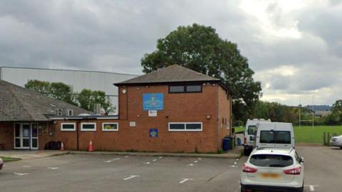 The front entrance of the rugby club with a view of the car park outside and a rugby pitch in the background