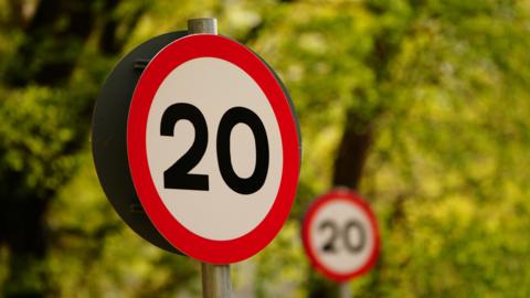 A 20mph sign with a woodland background