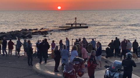 People stood looking out to sea from the UK's most easterly point in Lowestoft, with some motorcyclists in the foreground
