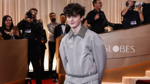 Owen Cooper, wearing a grey outfir, poses for photos at the Golden Globes award ceremony