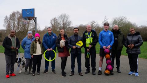 Six men, four women and a dog wearing coats and holding balls and other sports equipment