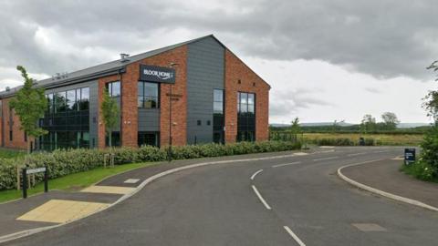 A two-storey Bloor 91ȱs office on a new road near a field on a cloudy day