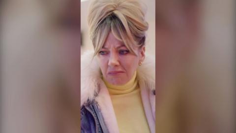 A woman looking disgusted, with blonde hair piled on top of her hair, and a coat with a fluffy collar.
