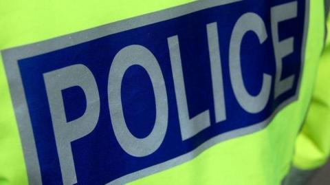 A close up of the back of a police officer's jacket showing the word "police" in capitals in silver letters on a dark blue background.