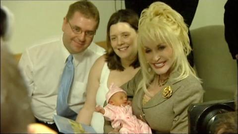Dolly Parton holds a baby next the mother and father