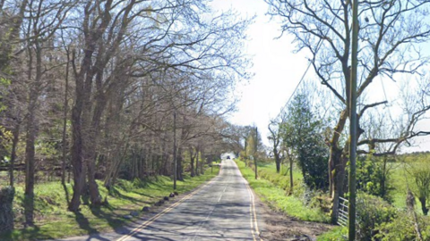 Small country road surrounded by woodland and with double yellow lines.