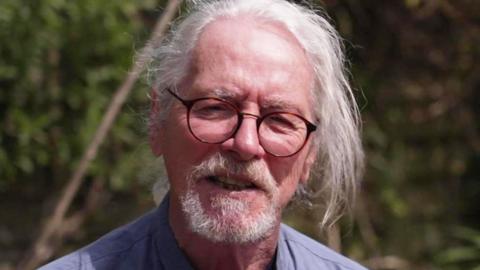 Headshot of Chris Burston - a man with grey hair and a grey beard and glasses.