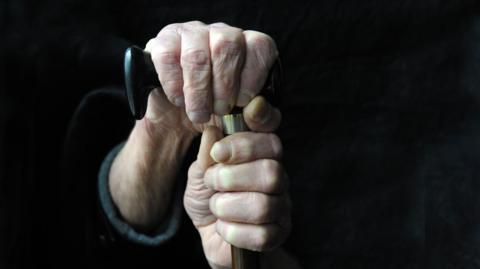 A stock image showing the hands of an elderly person holding a walking stick.
