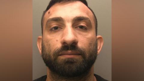 Police mug shot of Hristo Iliev. He has short dark hair and a beard and is looking directly at the camera.