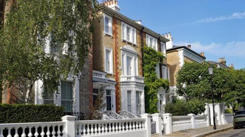 Elegant street of colourful old brick townhouses in the Chelsea district of London - the properties look to be large Georgian properties, with three floors