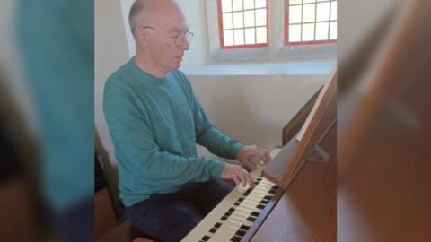 Mr Tomlinson in a blue jumper playing an electric organ