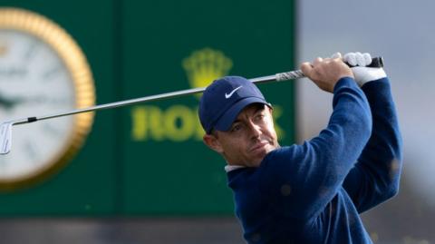 Rory McIlroy hitting a shot in front of a clock at Pebble Beach