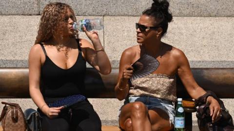 Two women sitting on a bench with fans in their hands
