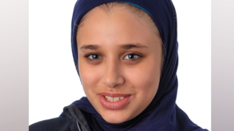 A headshot photo of Sara El-Khawas wearing a hijab and looking at the camera smiling against a white background.
