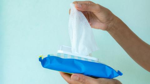 Someone holds a packet of wet wipes as they pull one from the packet
