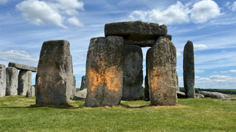 Stonehenge after it was sprayed with an orange substance during a Just Stop Oil protest. Three of the stones are covered with the substance. 