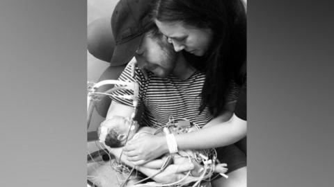 Quinn Parker's parents holding the baby. It's a black and white picture.