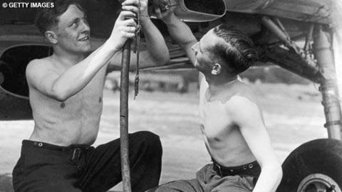 Two men try to fix part of the underside a plane.