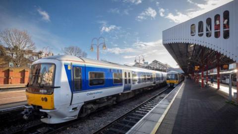 A white and blue train at a rail station on a sunny day