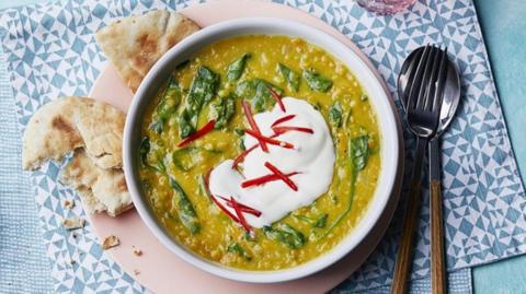 Coconut dal topped with a scoop of yoghurt and pitta on the side