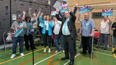 Celebrating men and women with their arms raised in the air in a sports hall