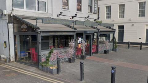 Streetview of the Wafi Lounge, it is a grey building with a glass conservatory-style section wrapping around the building.