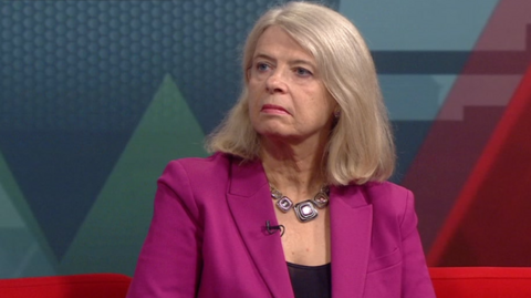 MP Dame Harriet Baldwin, a woman with shoulder-length light blonde hair, sits in the ý Politics Midlands studio on a red sofa, while wearing a purple jacket and necklace