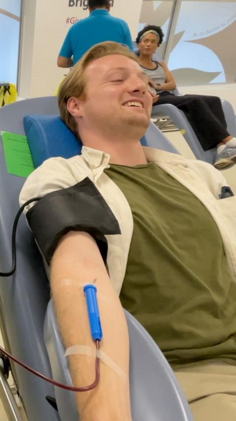 Young man in a green t-shirt lying down giving blood with tube connected to arm
