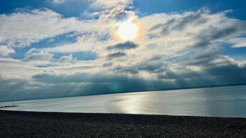 A beach scene with the sun low in the sky and the light quickly fading. There is a little blue sky but lots of cloud across the sky. The beach is empty.